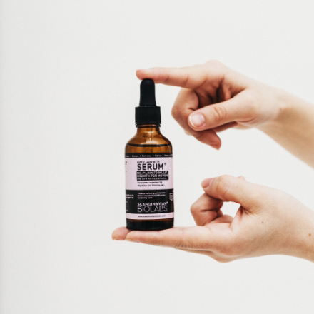 Bottle of hair serum held between two hands, featuring Scandinavian Biolabs branding and product details, relevant to hair care and styling.