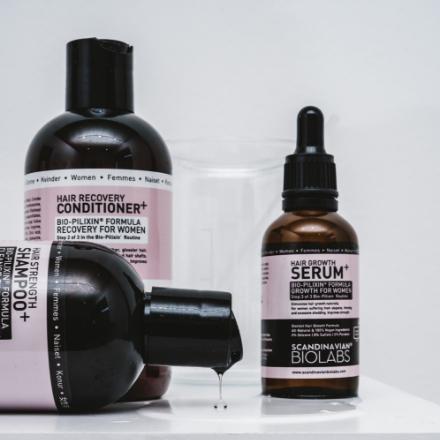 Hair care products including conditioner and serum from Scandinavian Biolabs, featuring pink labels and black containers, displayed on a white surface.