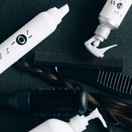 Hair care products and combs arranged on a dark surface, featuring styling sprays and tools relevant to African braiding hairstyles at La Belle African Braids.