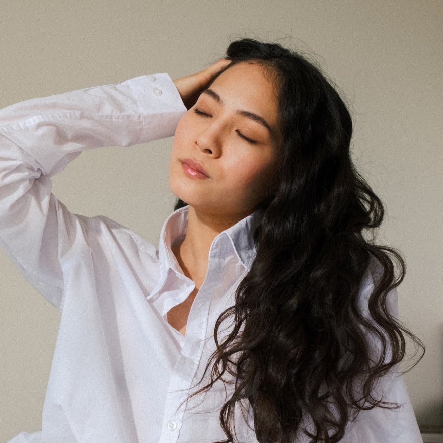 Young woman with long, wavy hair wearing a white shirt, showcasing a casual hairstyle in a relaxed pose.